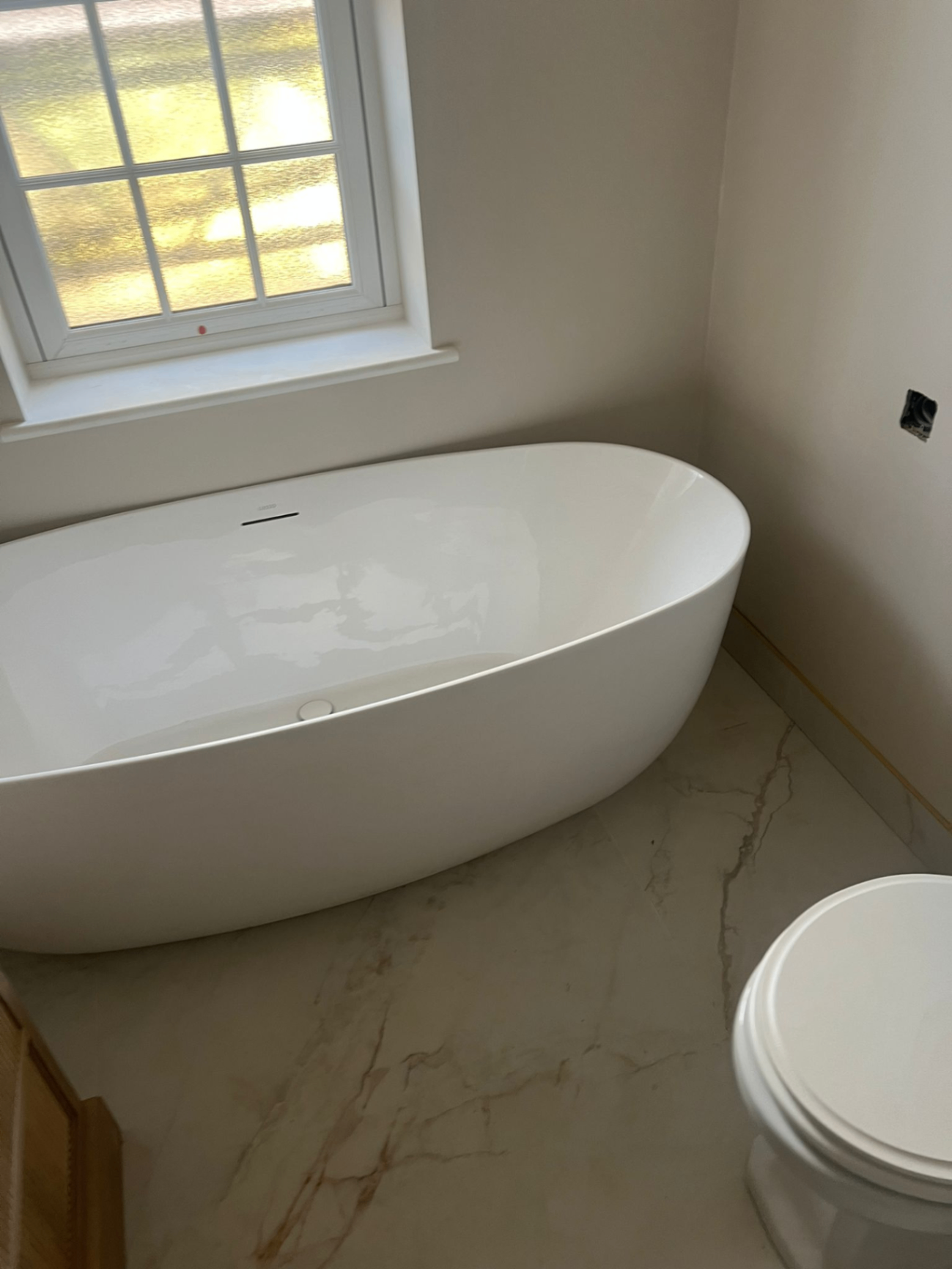 Freestanding oval bath on veined marble floor with brass detail trim — Avanza bathroom, Essex