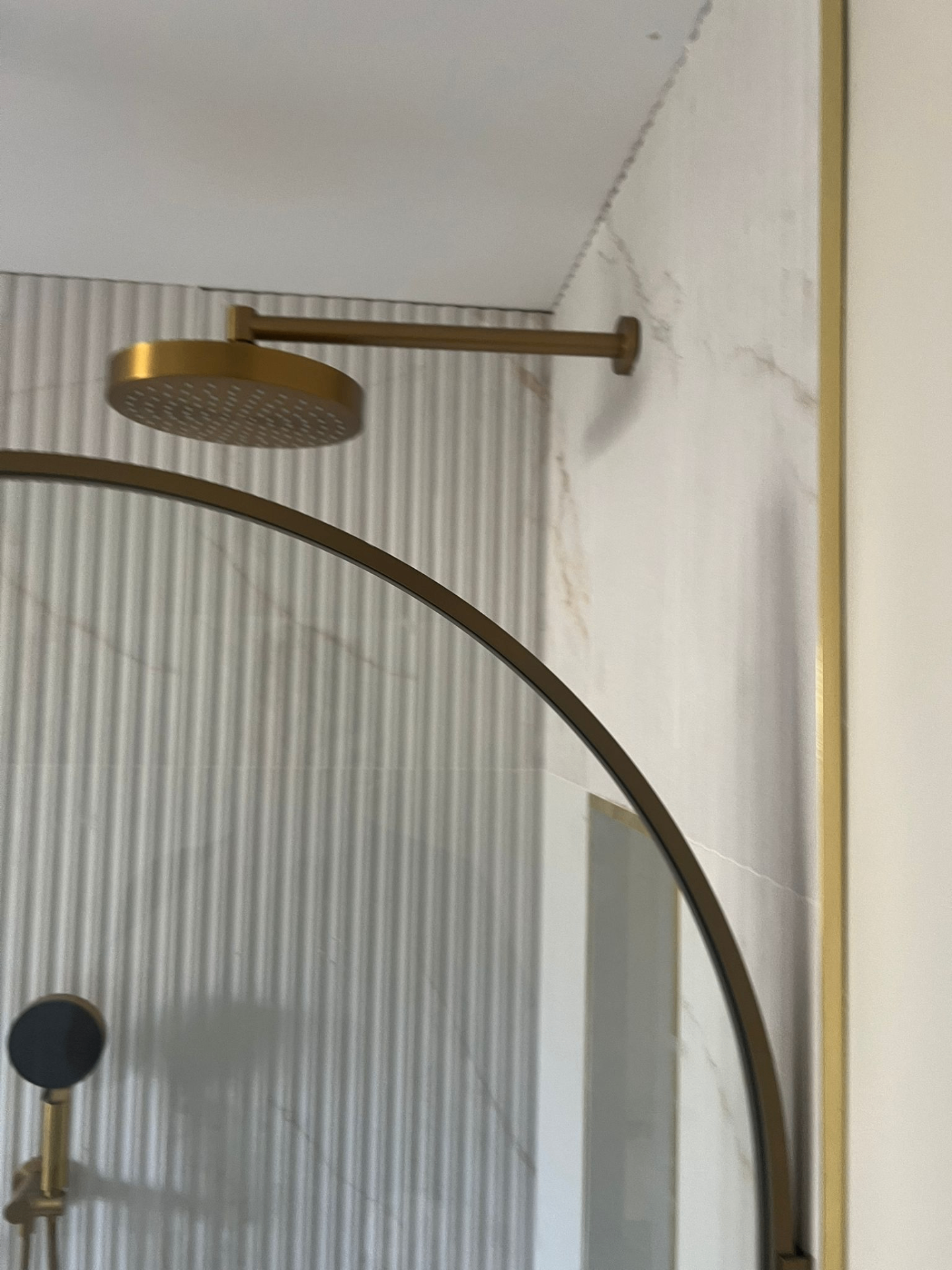 Brass rain shower head over fluted marble tiles with curved brass shower screen — Avanza project, Essex