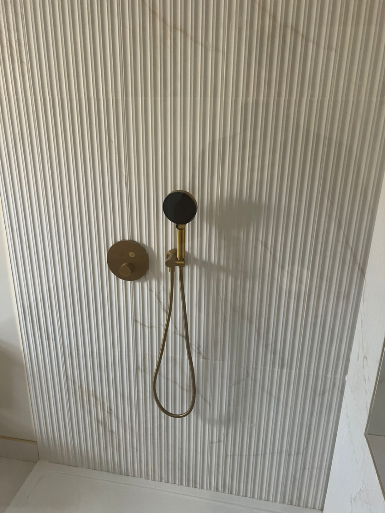 Brass shower valve and handset on reeded marble feature wall — Avanza bathroom, Essex